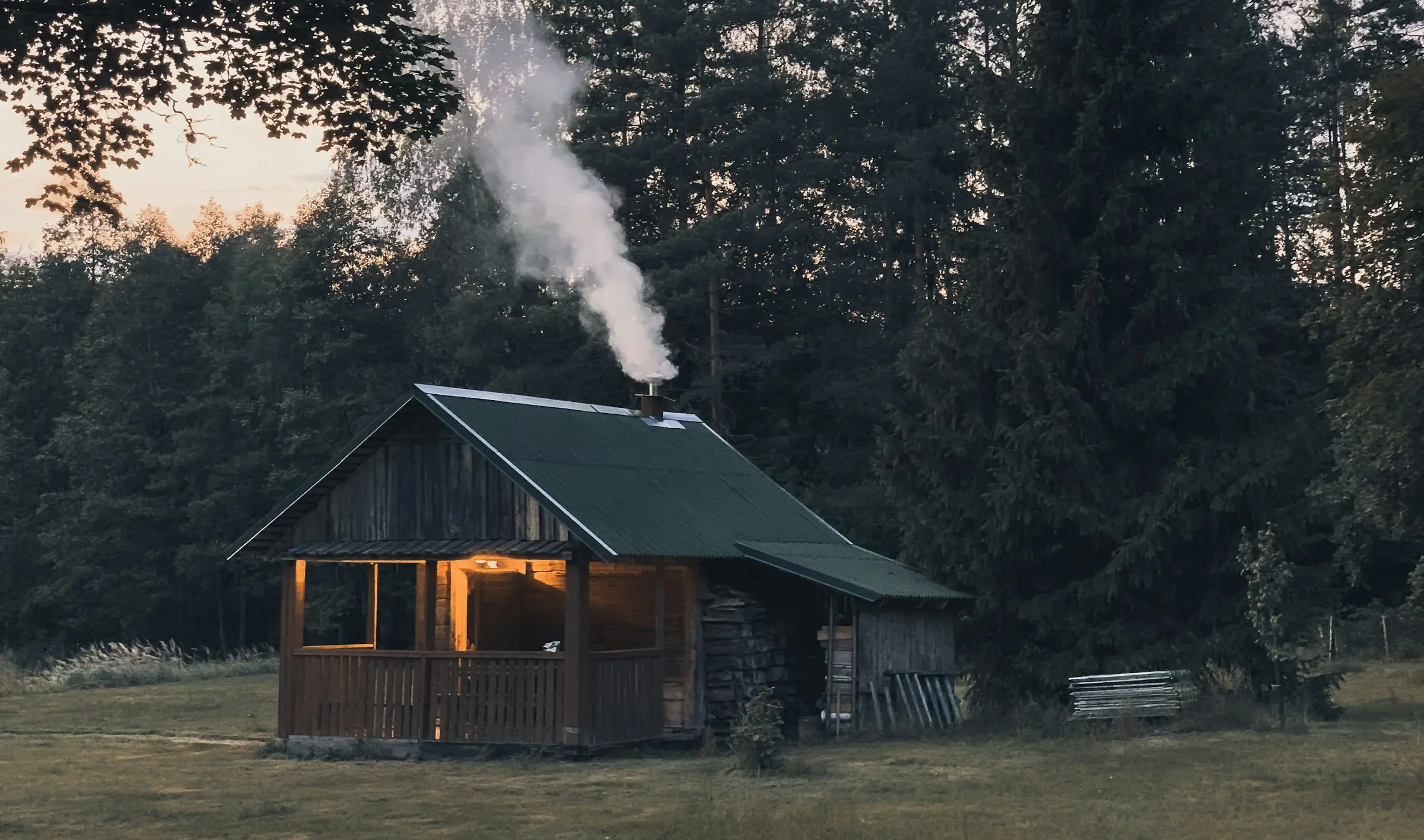 Cabaña de madera con humo saliendo de la chimenea, al borde de un bosque