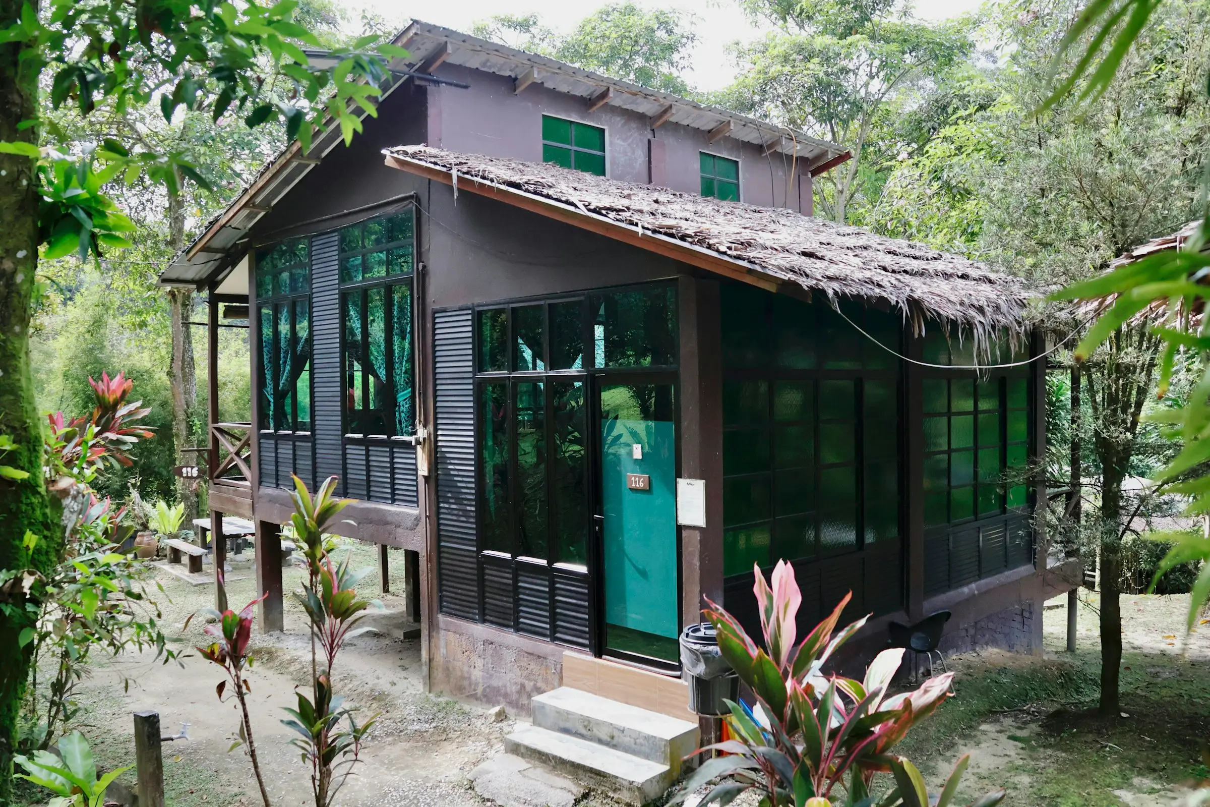 Casa de madera con ventanales en medio de un jardín tropical