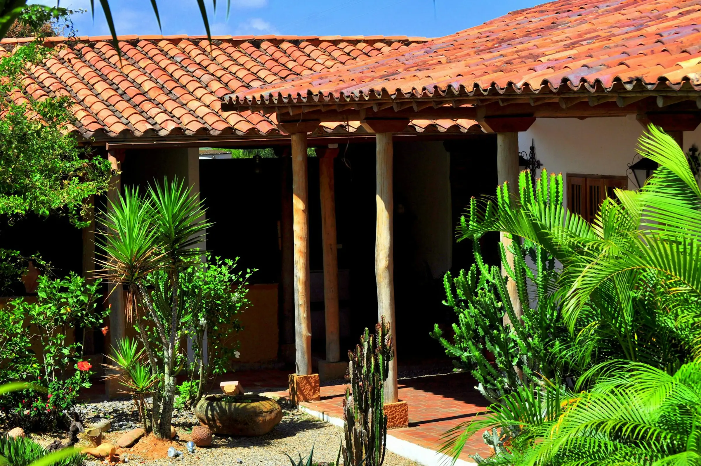 Casa con techo de teja de barro y jardín de plantas tropicales en Barichara
