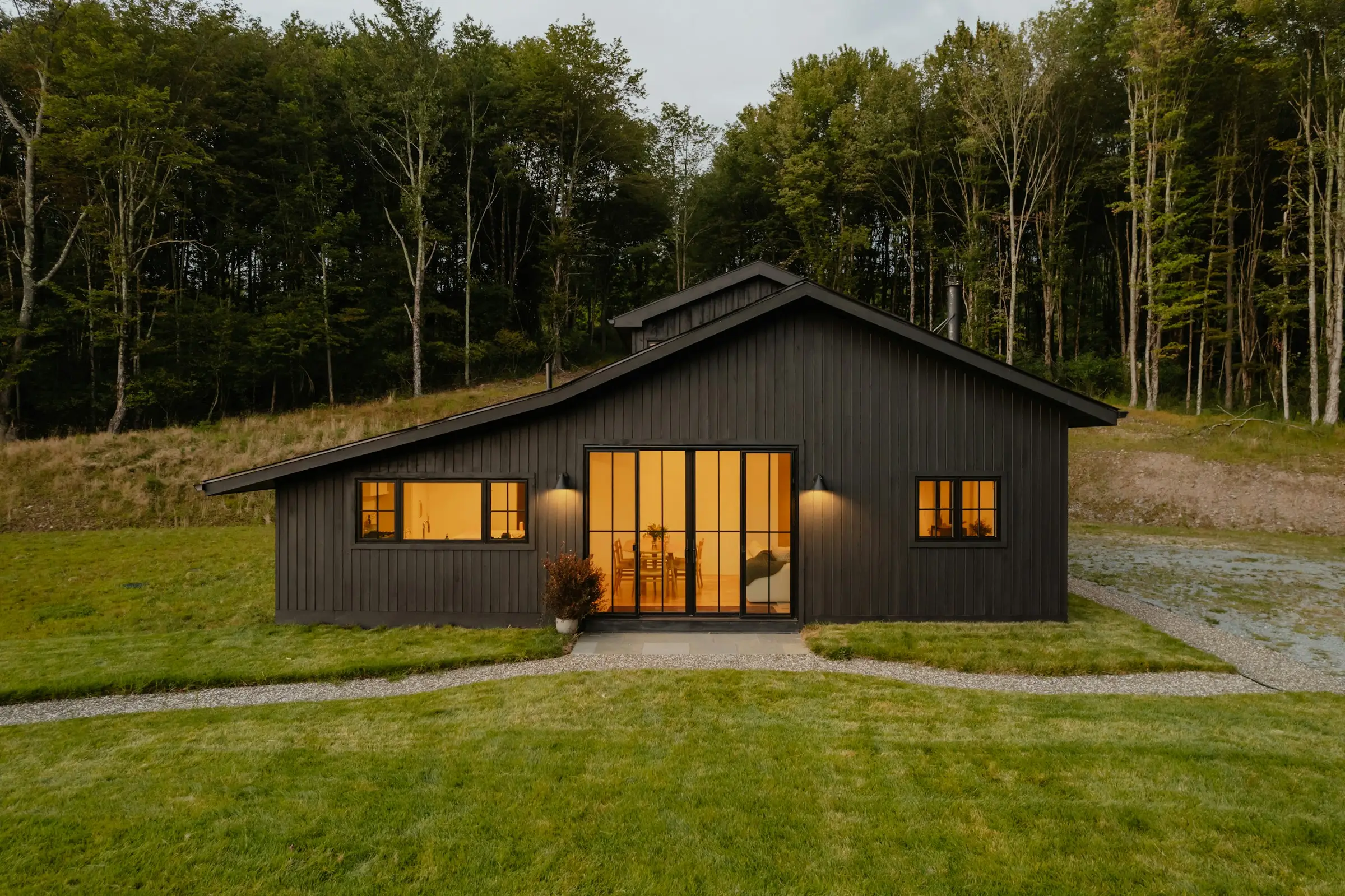 Chalet moderno de madera oscura con ventanales iluminados, frente a un prado