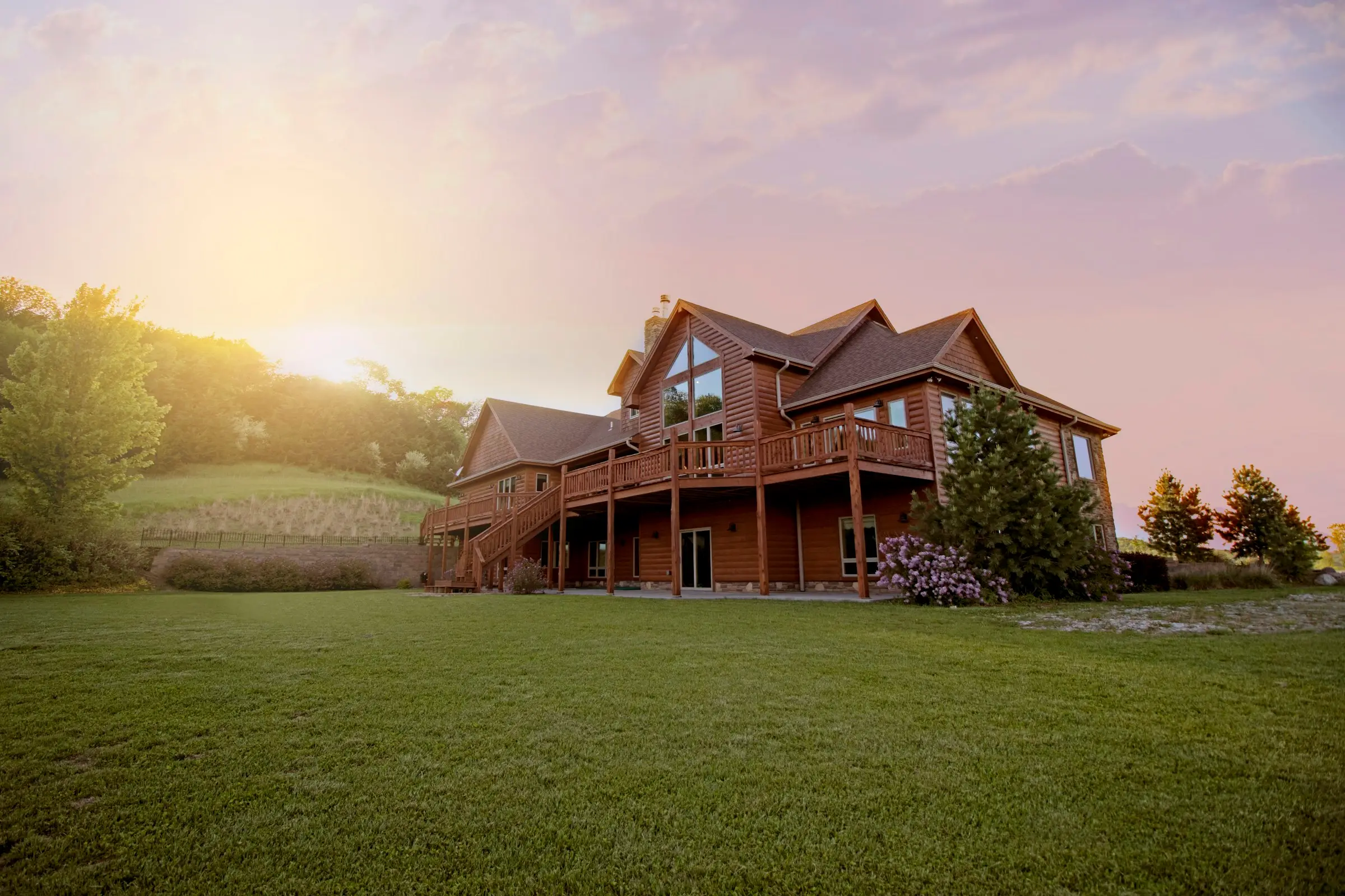 Casa grande de madera con terrazas al atardecer, frente a un prado