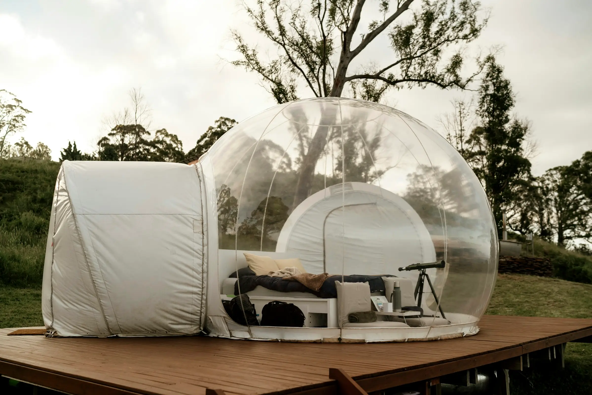 Domo burbuja transparente con cama y túnel de entrada, sobre una terraza de madera