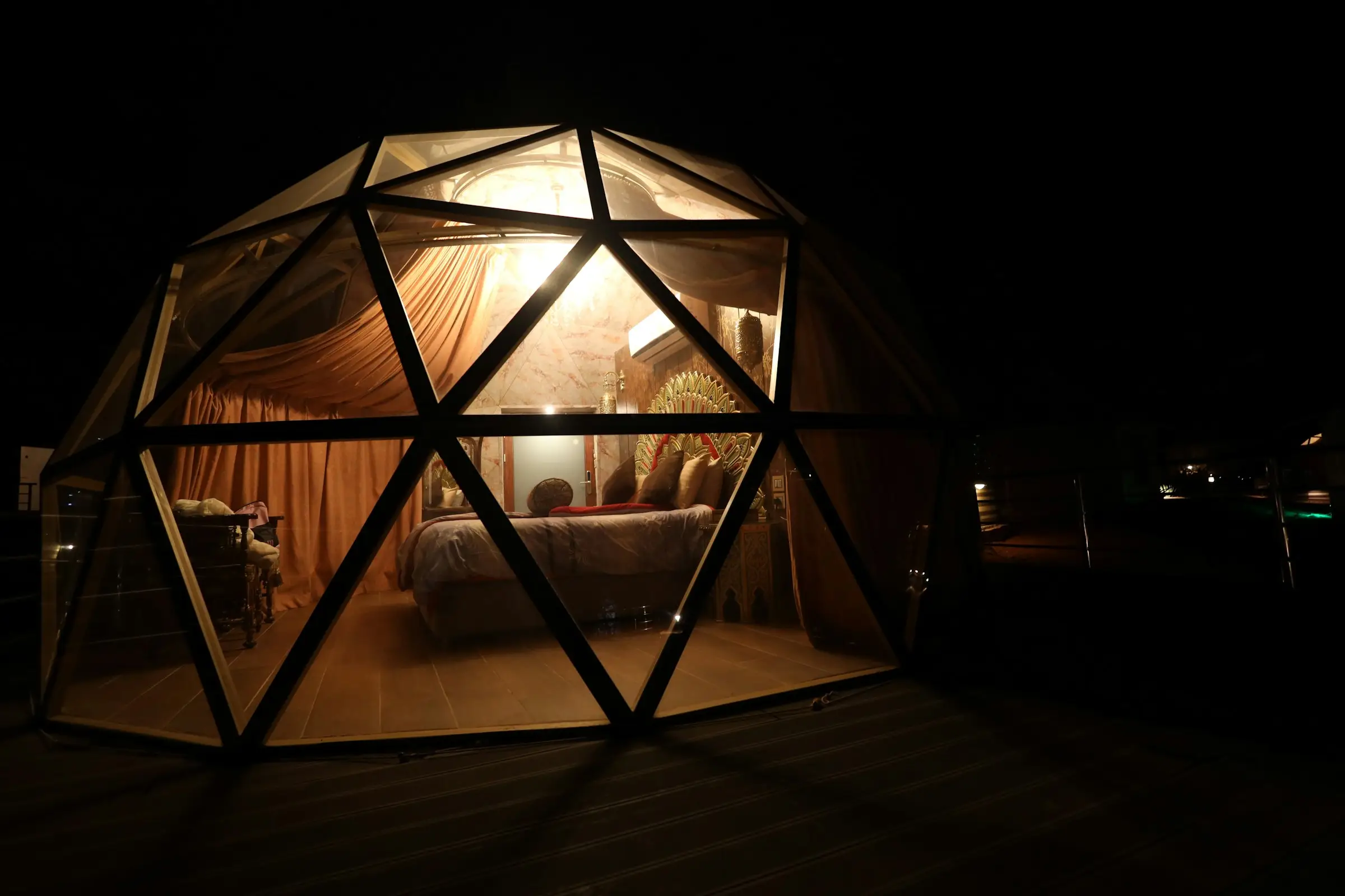 Domo geodésico iluminado por dentro en la noche, con la cama visible a través de la estructura