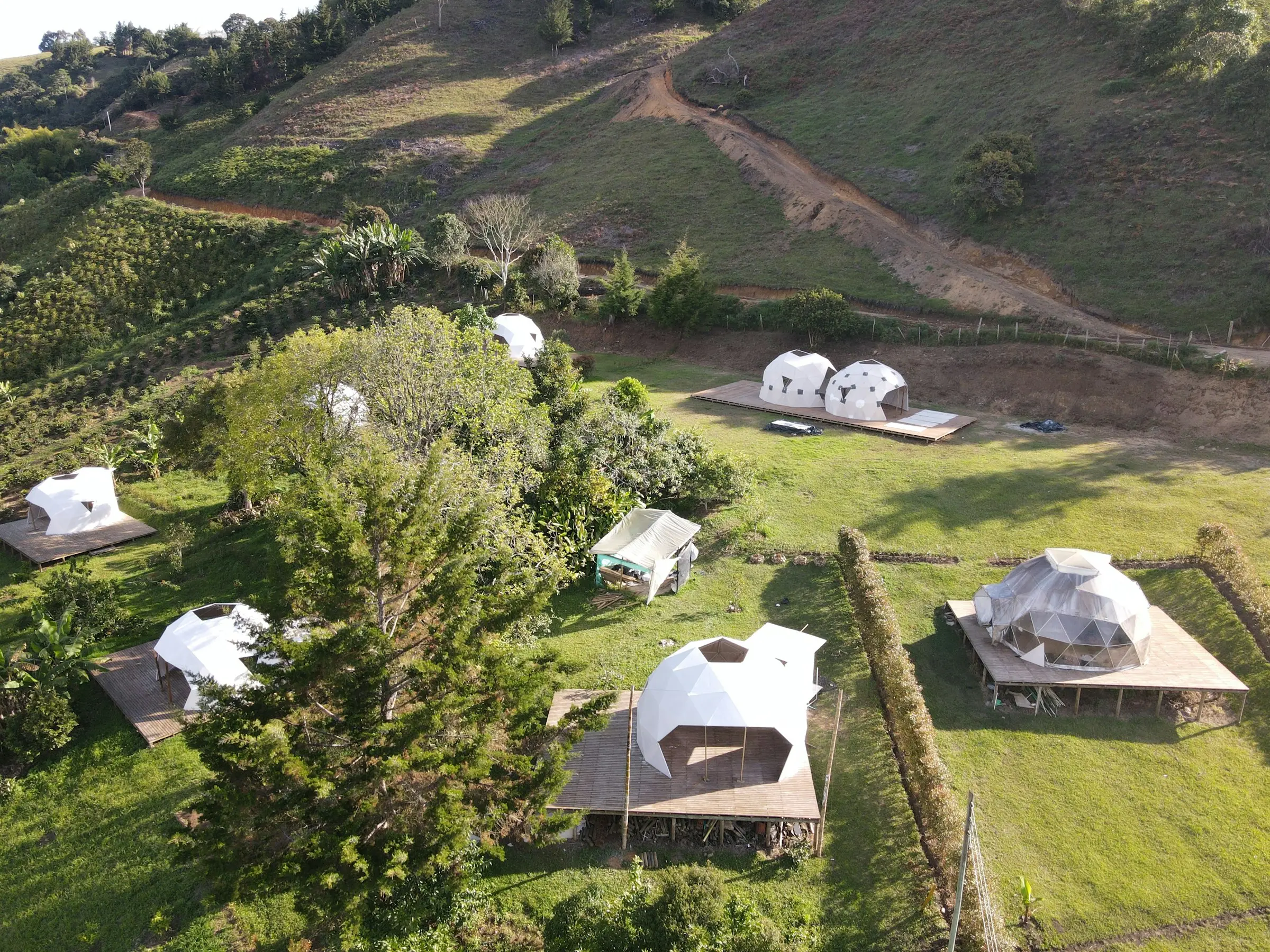 Vista aérea de varios domos con terraza repartidos en un terreno verde de montaña