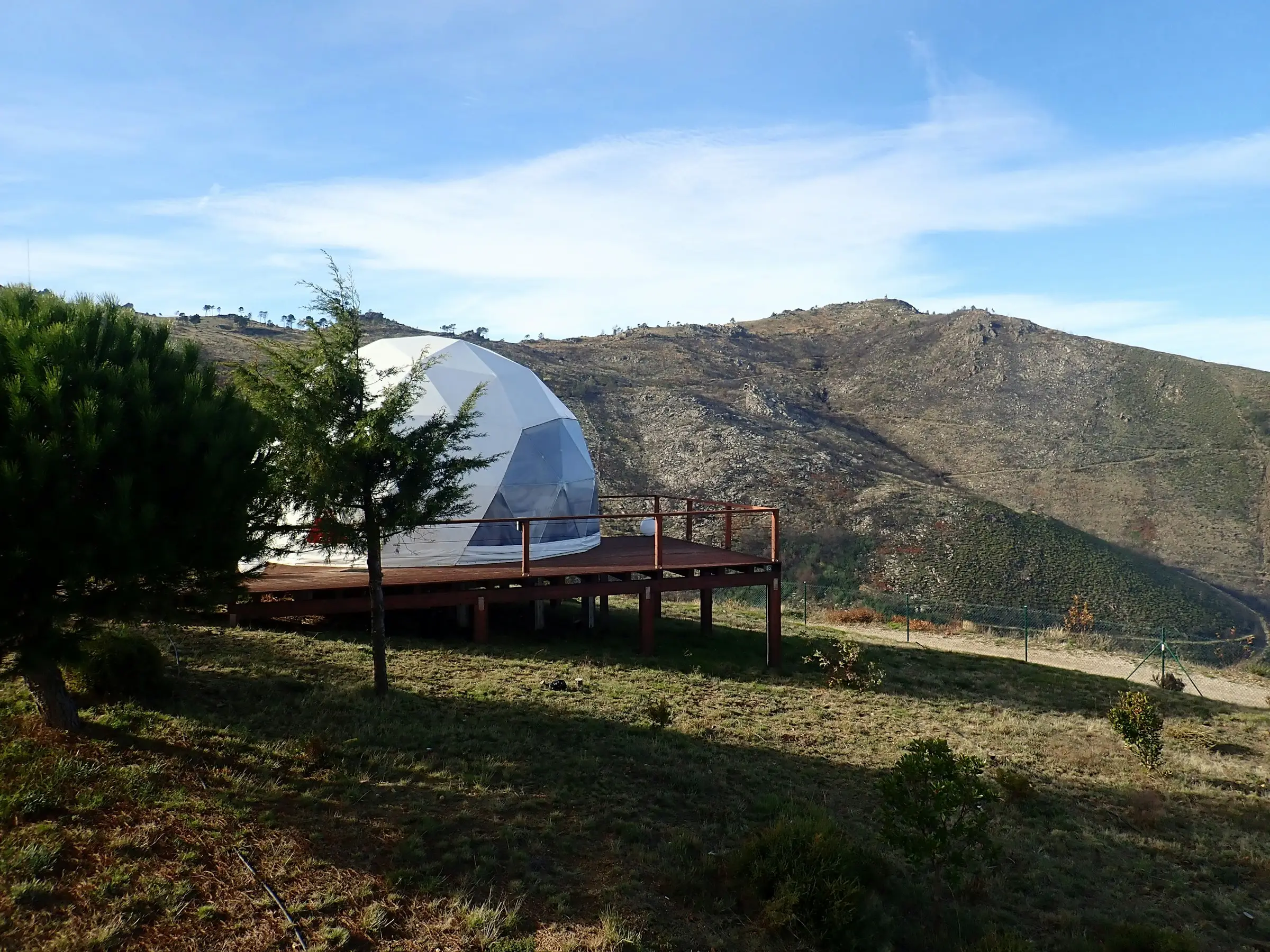 Domo blanco sobre una terraza de madera en una ladera, con montañas al fondo