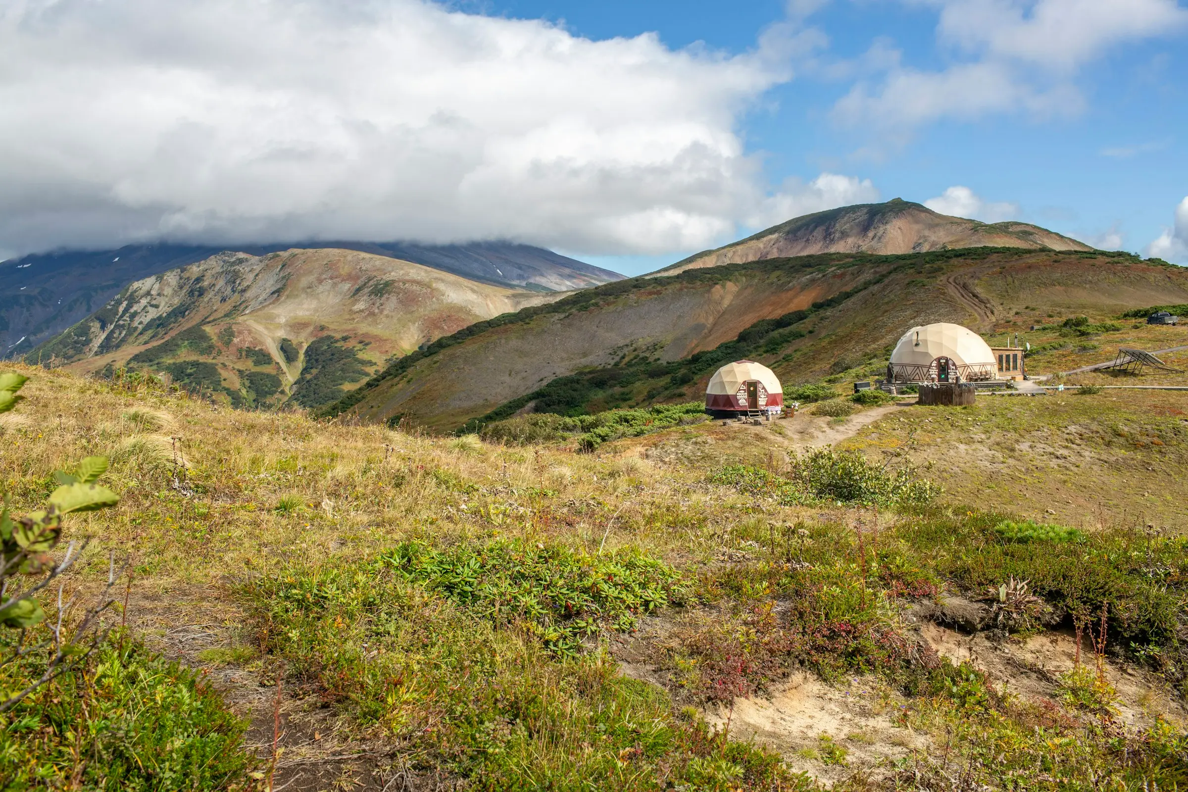Dos domos geodésicos en una ladera de pasto con montañas alrededor