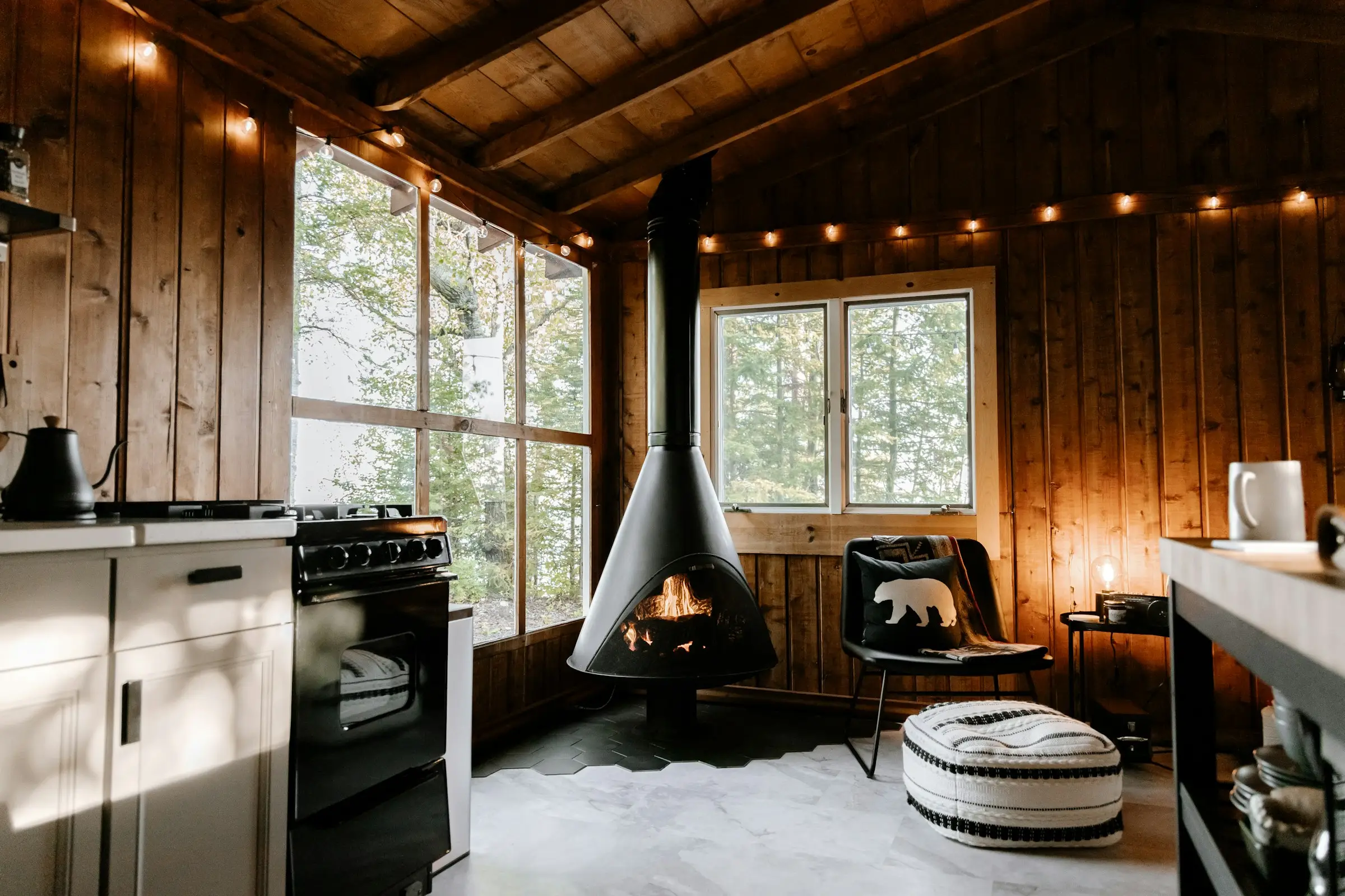 Sala de una cabaña de madera con chimenea colgante y luces cálidas