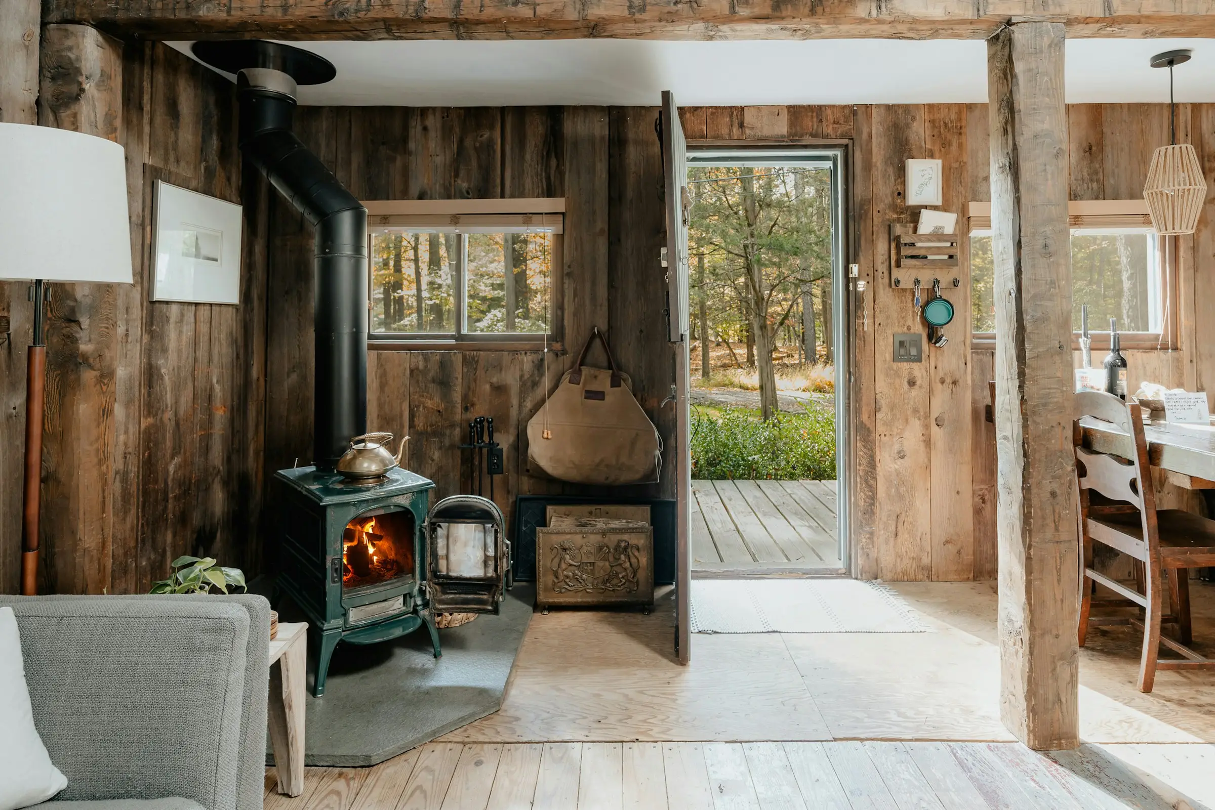 Sala rústica de madera con estufa de leña y la puerta abierta hacia el bosque