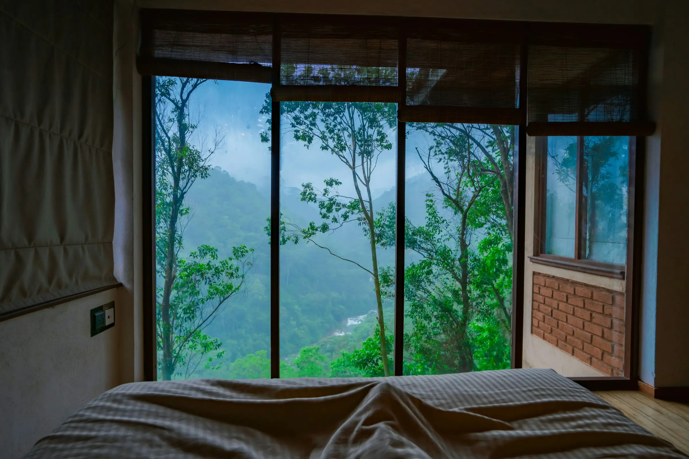 Habitación con ventanal frente a montañas verdes cubiertas de niebla