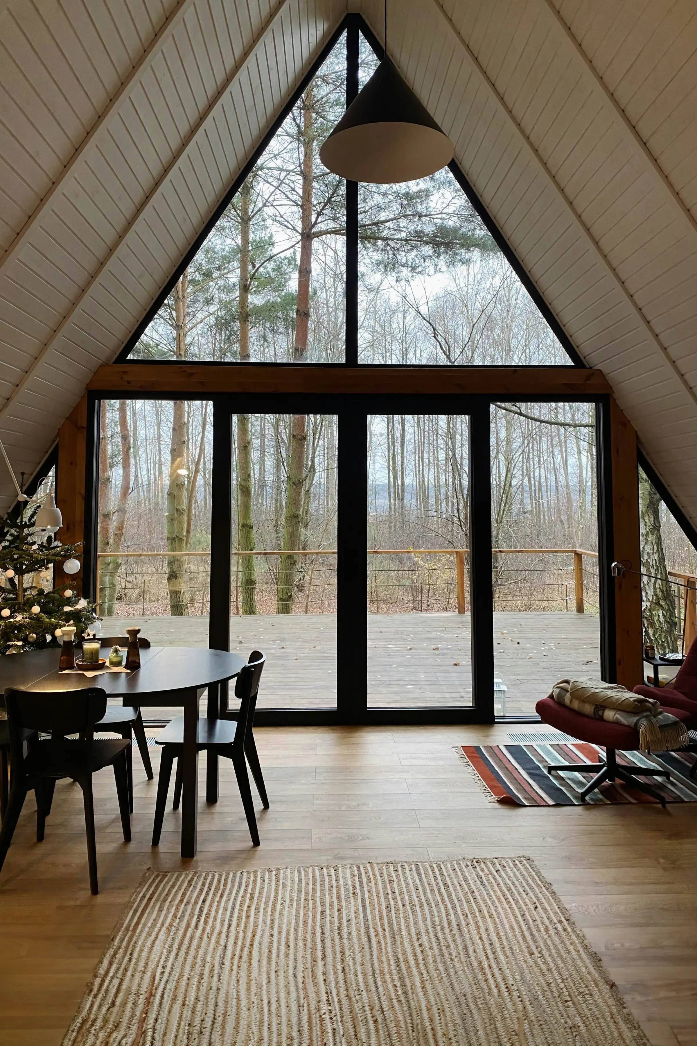 Interior de una cabaña A-frame con comedor frente a un gran ventanal hacia el bosque