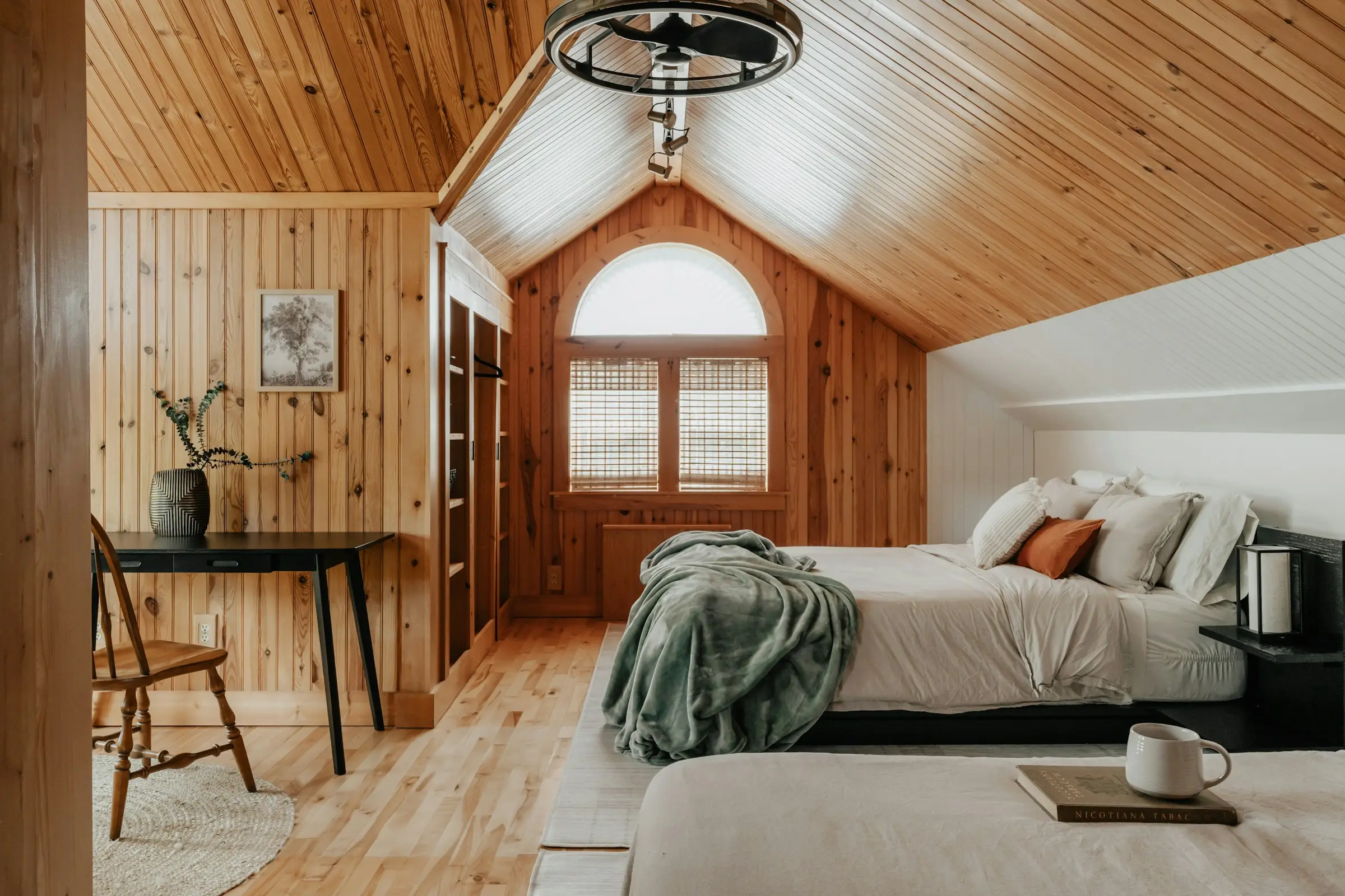 Habitación de madera bajo el techo inclinado, con cama y ventana en arco