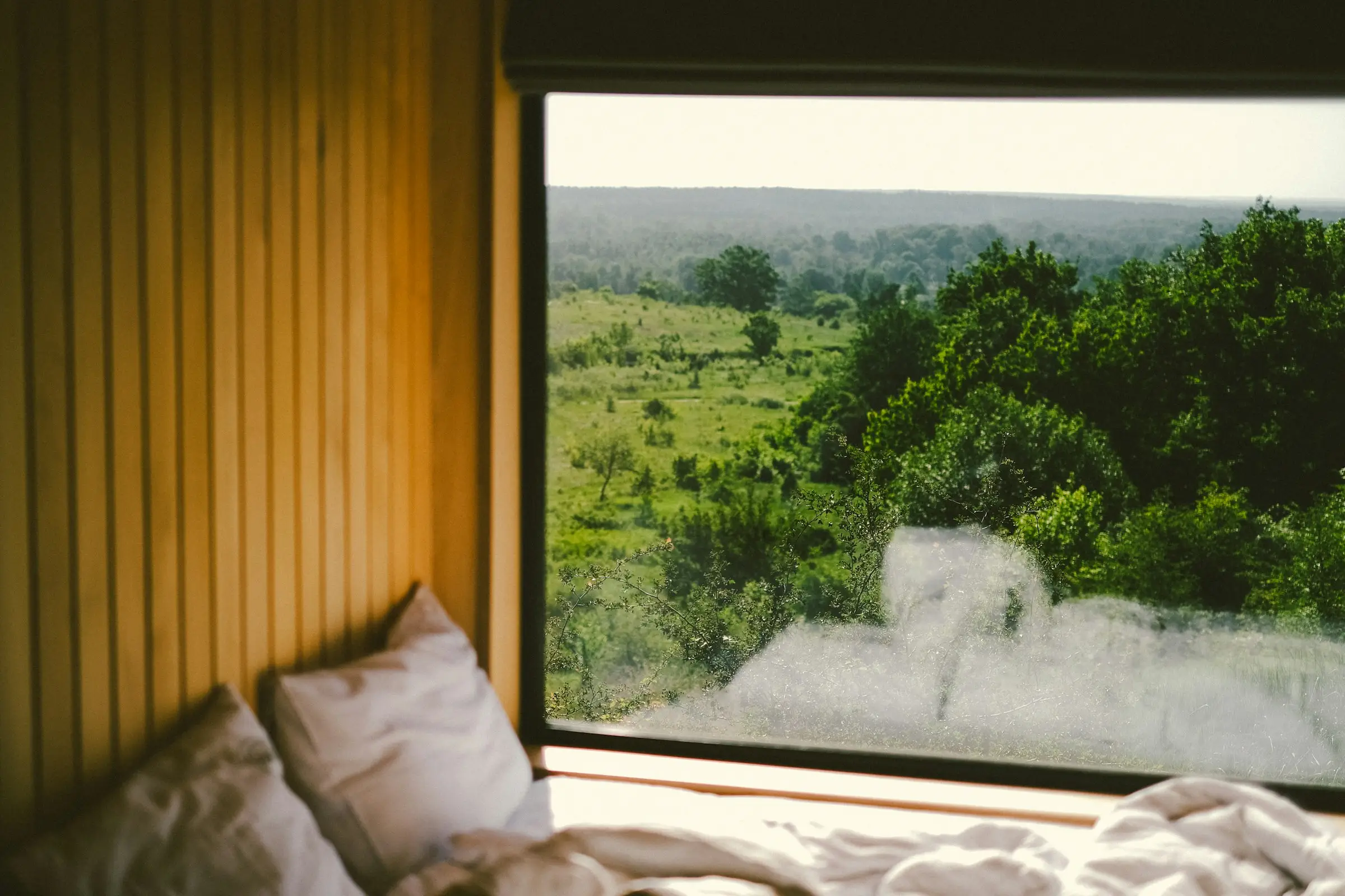 Cama junto a una ventana grande con vista a un paisaje verde