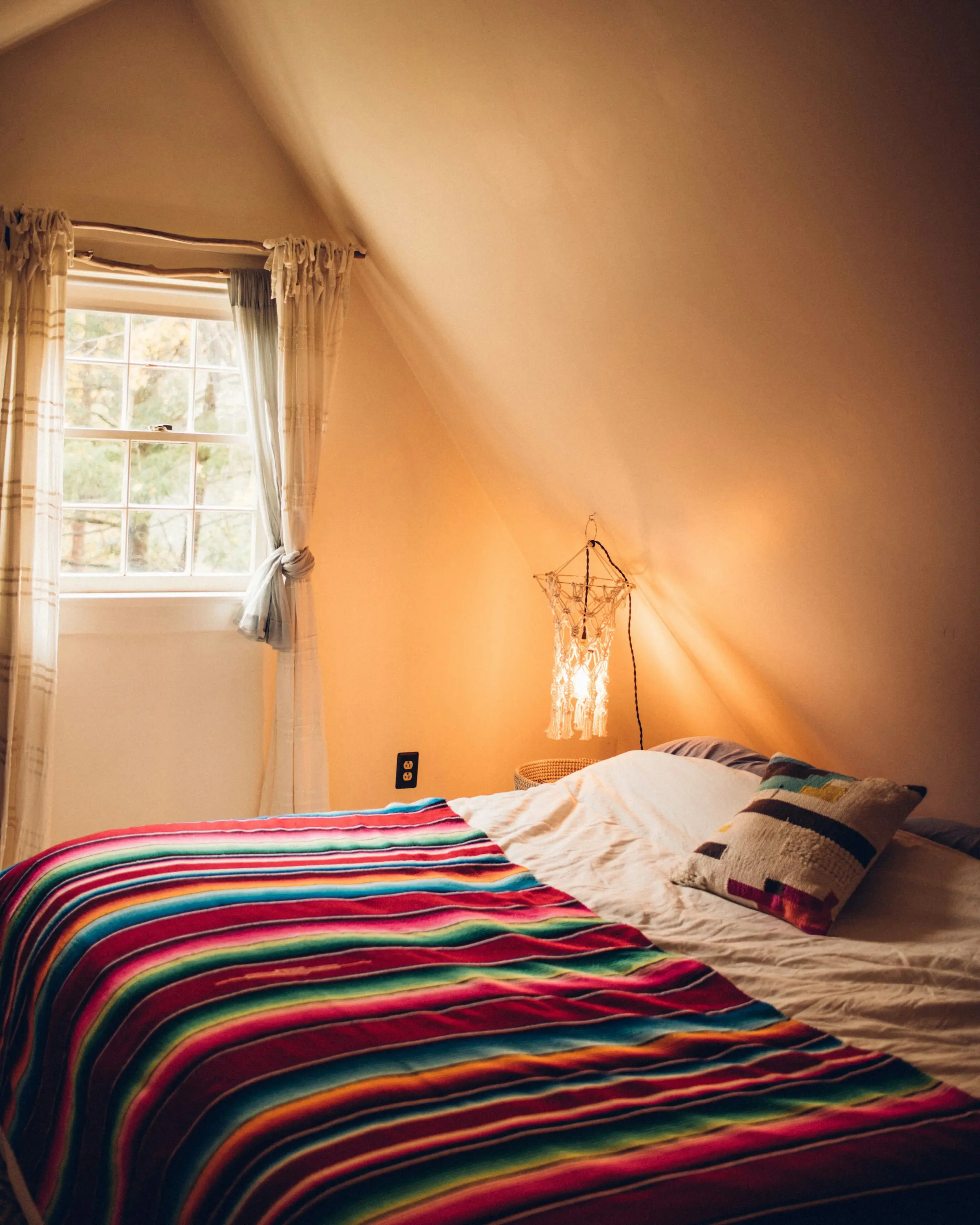Cama con cobija de rayas bajo el techo inclinado de una cabaña