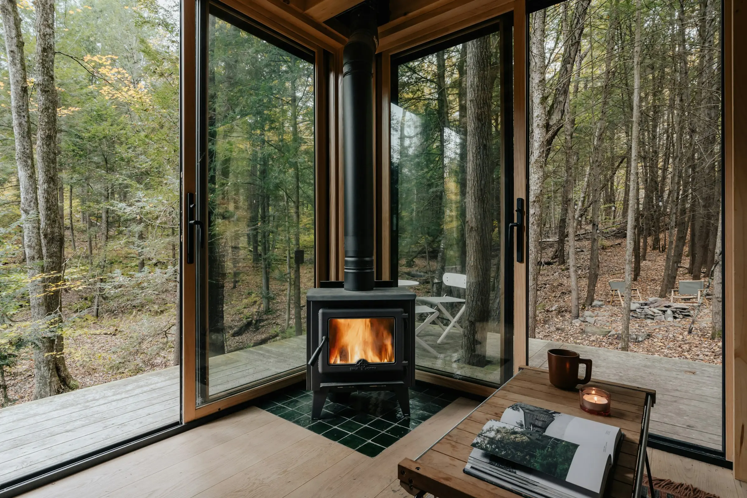 Sala con estufa de leña y paredes de vidrio frente al bosque