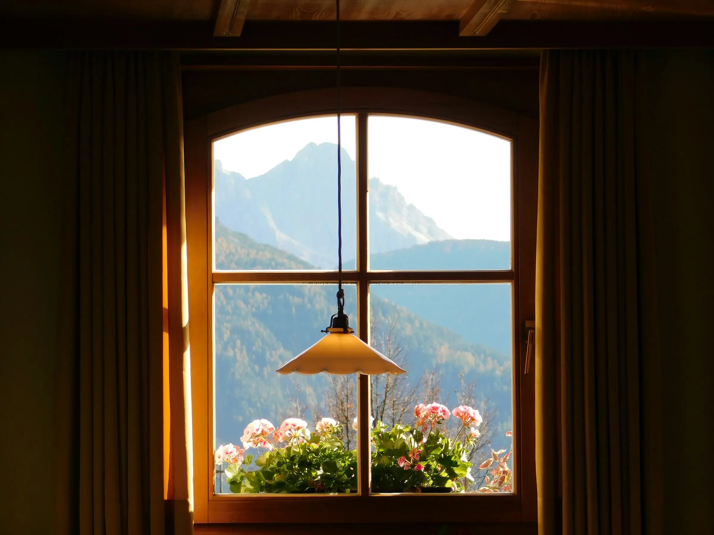 Ventana de madera con flores y una lámpara, abierta hacia las montañas