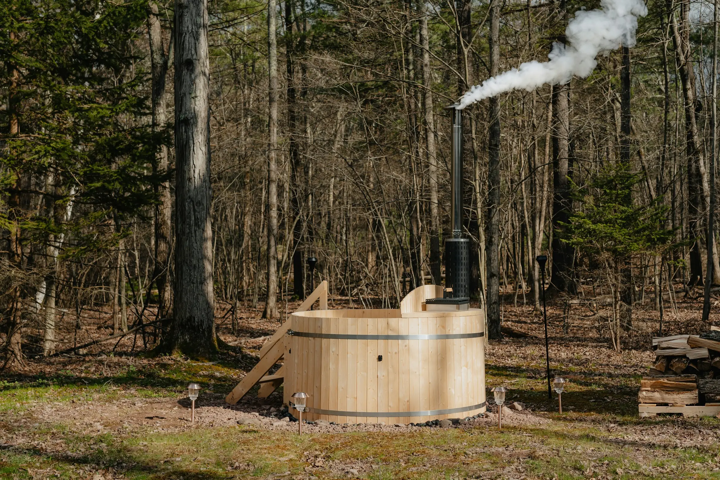 Tina de madera con chimenea humeante en medio del bosque