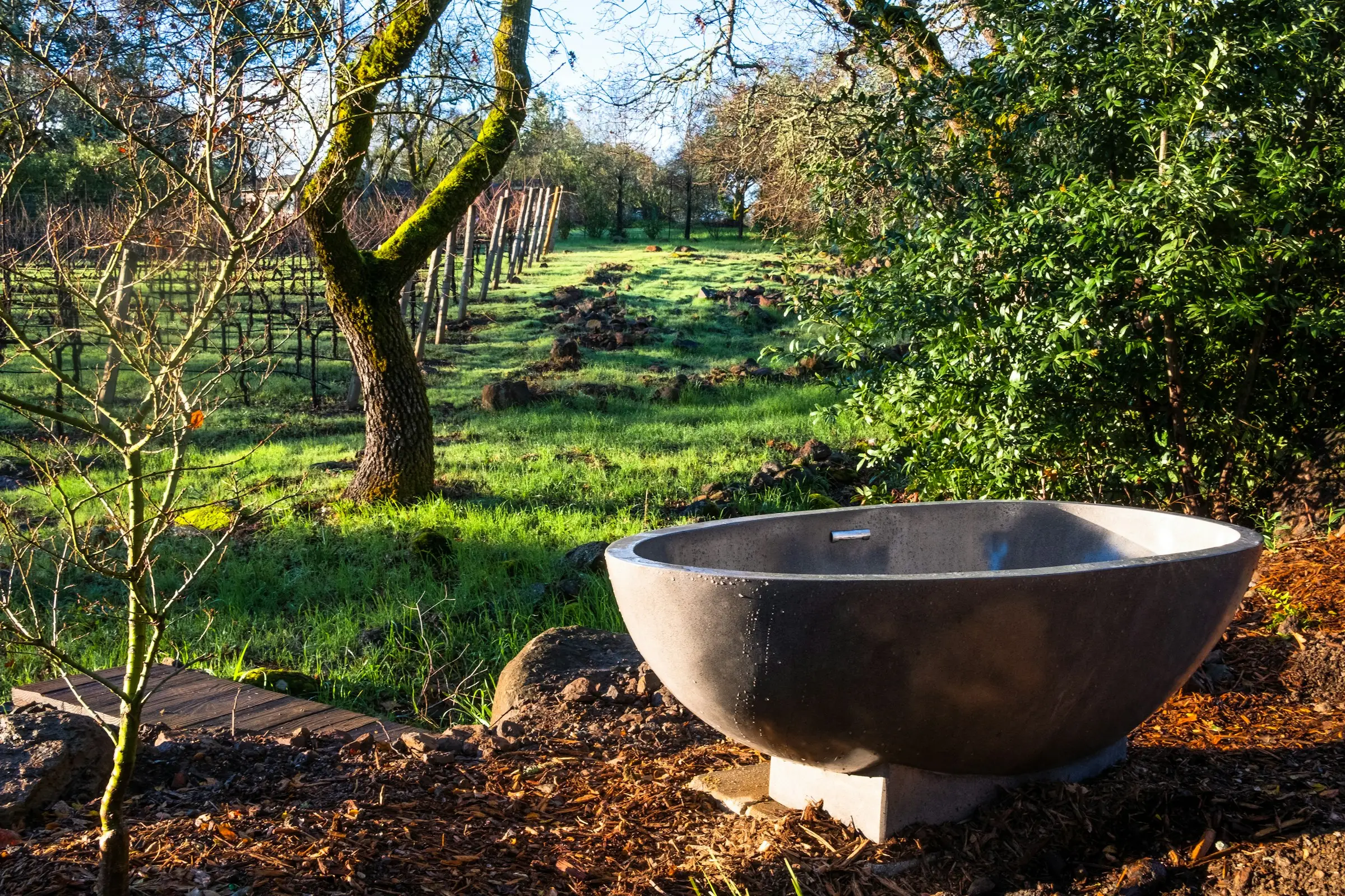 Bañera de piedra al aire libre en un jardín verde con árboles