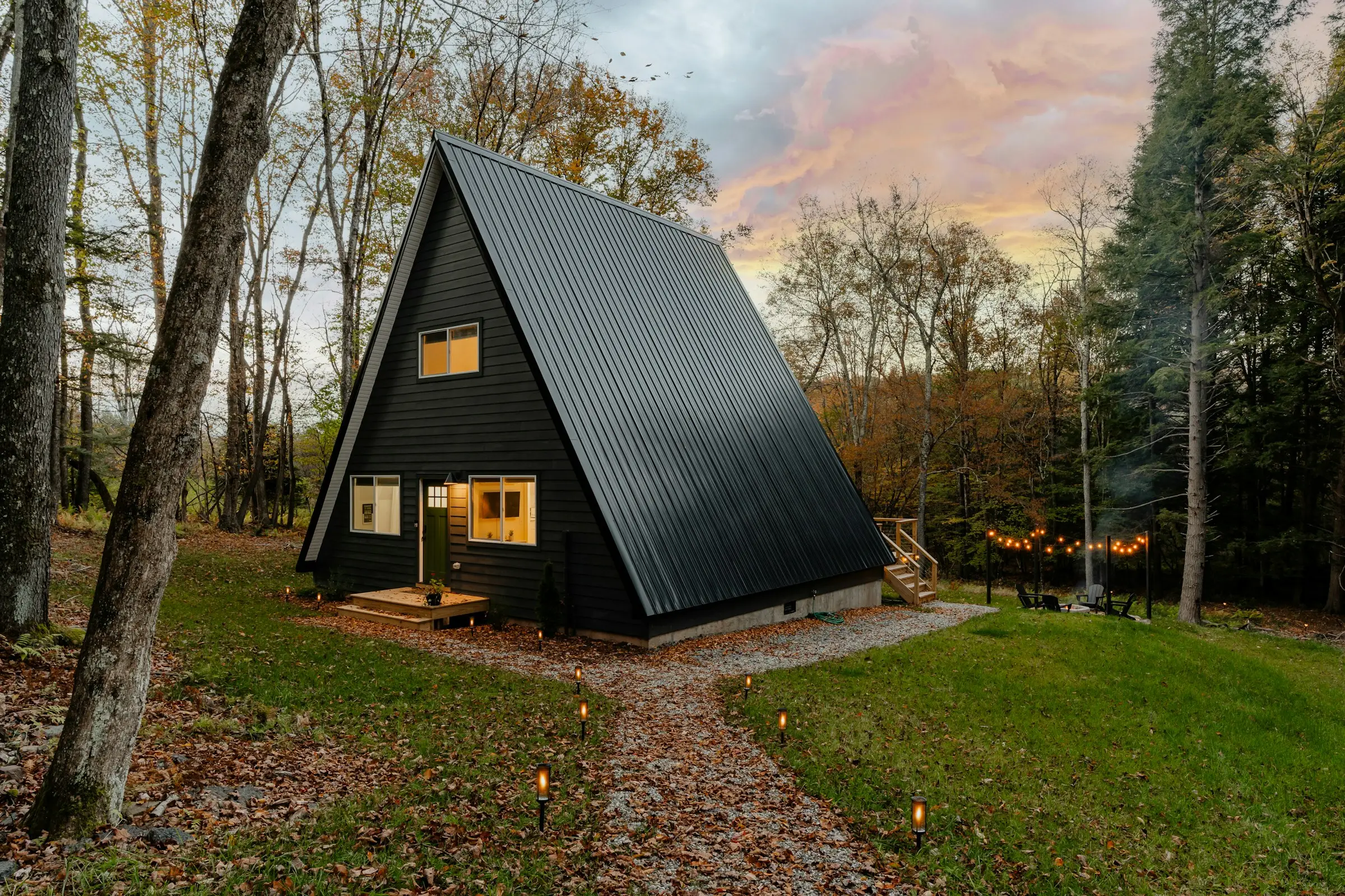 Cabaña A-frame negra entre árboles, con el cielo del atardecer