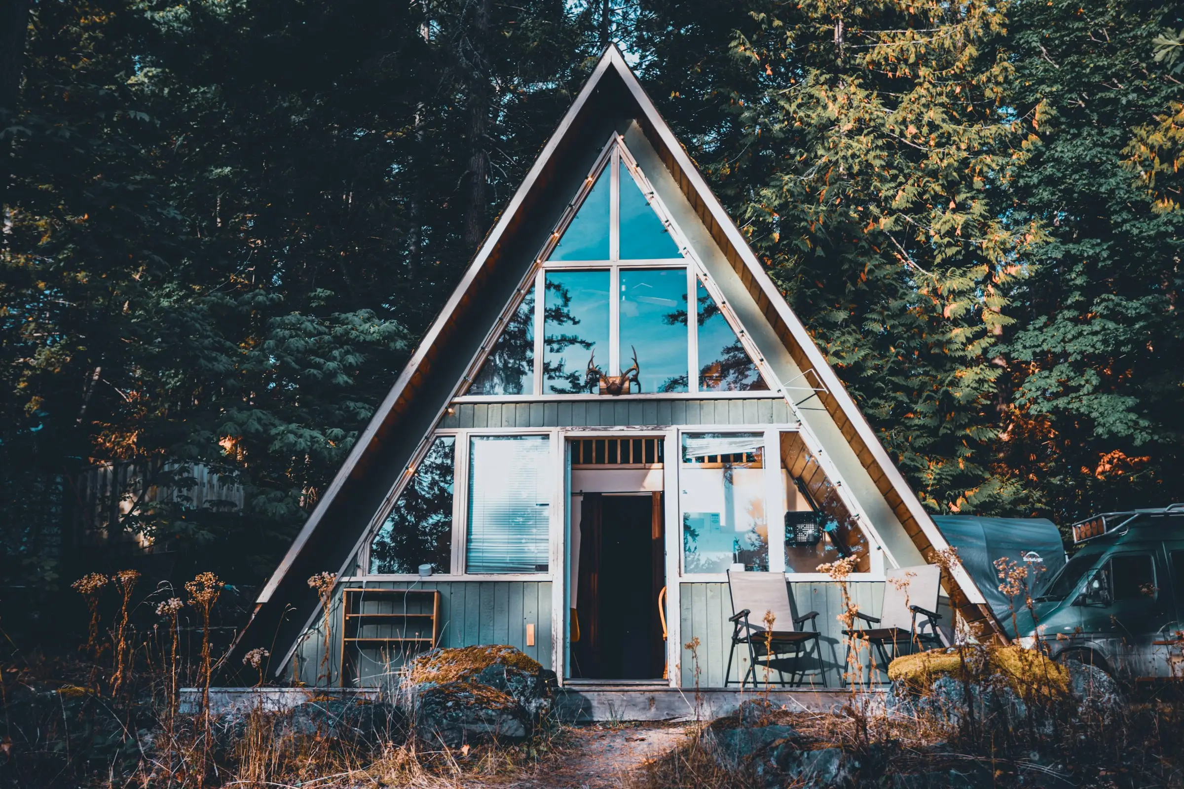 Cabaña A-frame con fachada de vidrio iluminada en medio del bosque