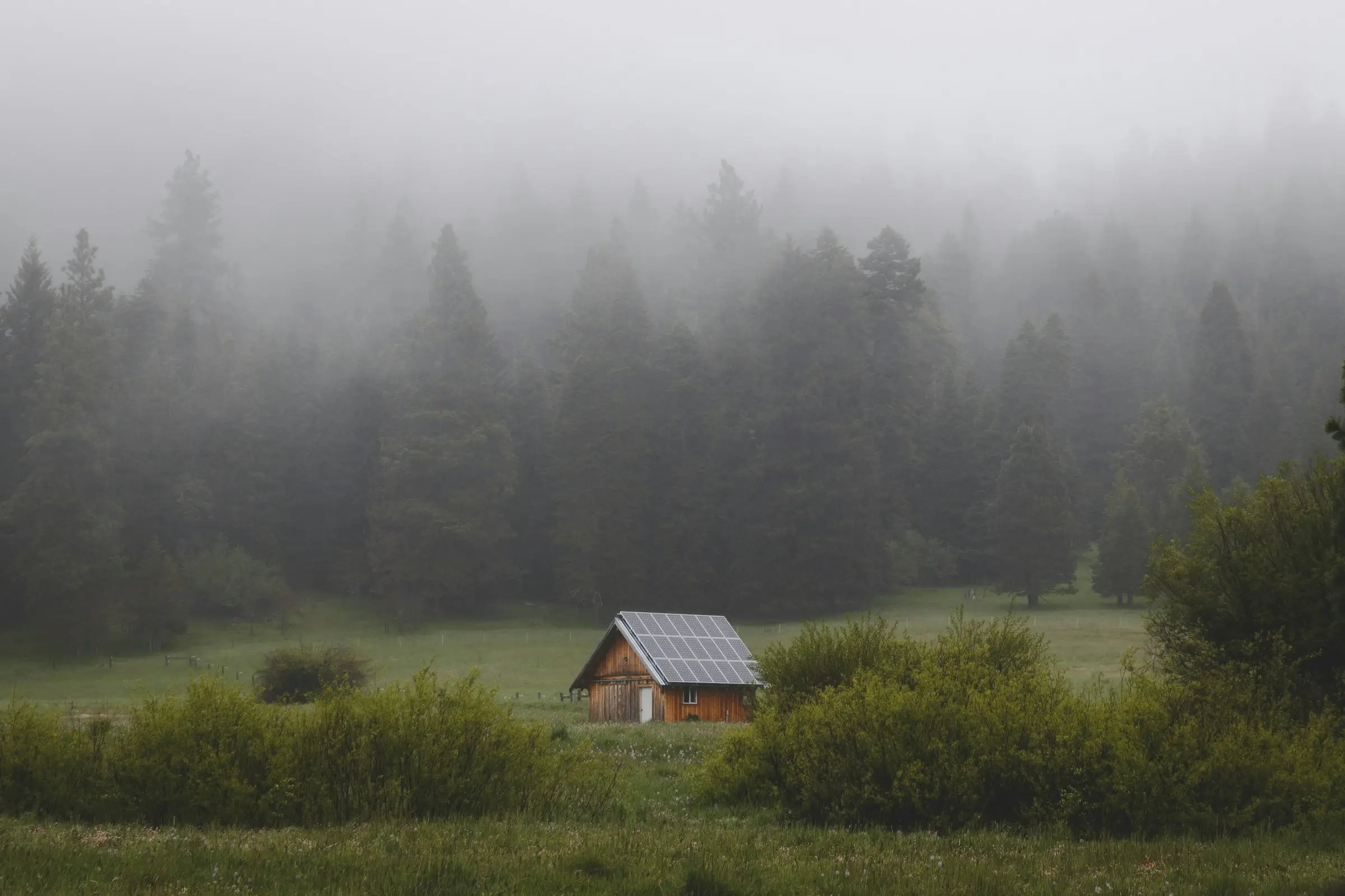 Cabaña pequeña con paneles solares en un prado con niebla