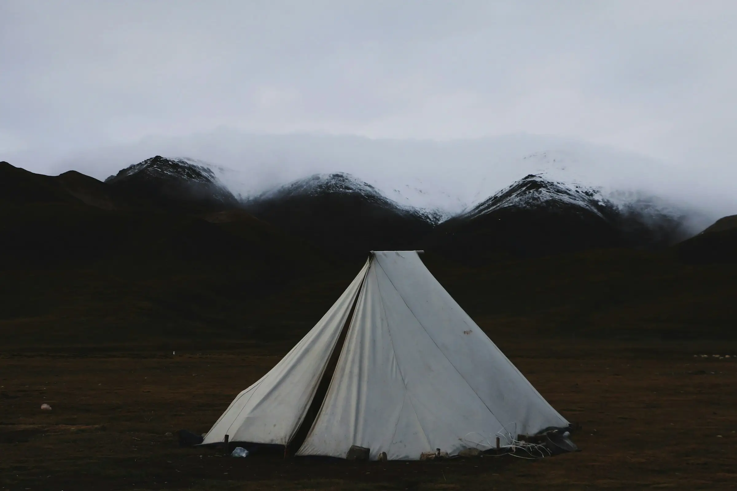 Tipi blanco en un campo abierto, con montañas oscuras y nubes al fondo