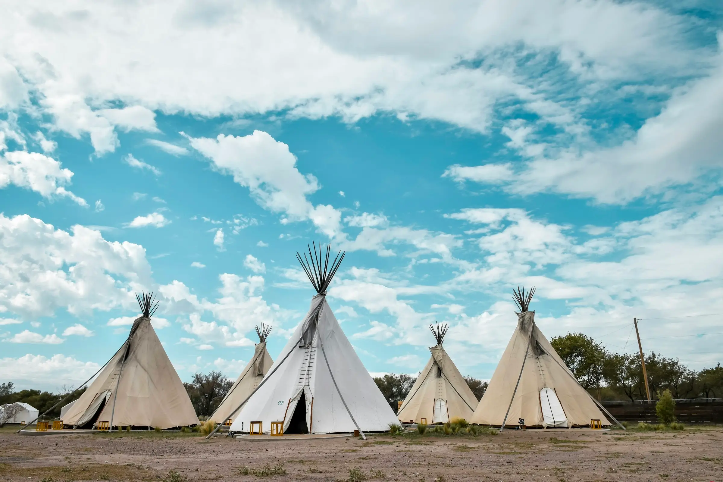 Cinco tipis blancos bajo un cielo azul con nubes